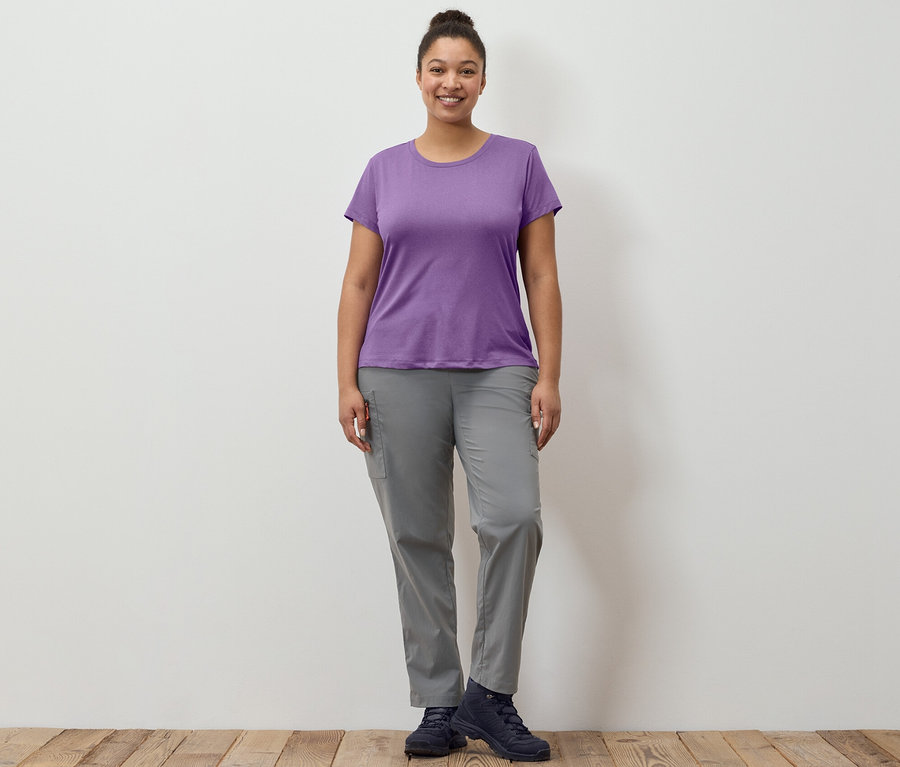 Žena stojí a má na sebe sivé zbaliteľné turistické nohavice a strečové funkčné tričko.