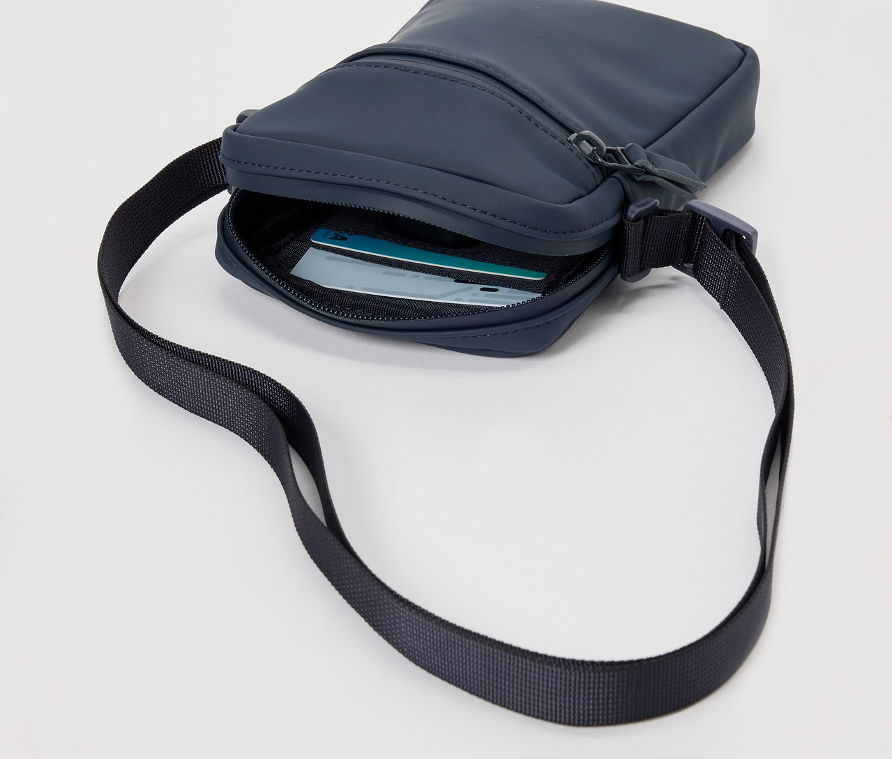 Tmavo modrá taška na rameno do dažďa s čiernym popruhom a kartami vnútri.