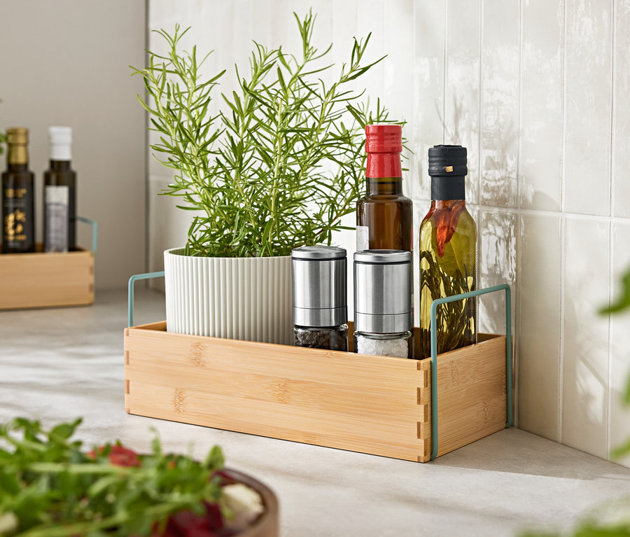 Bylinky v kvetináči, dva mlynčeky na korenie a dve fľaše oleja v drevenom podnose.