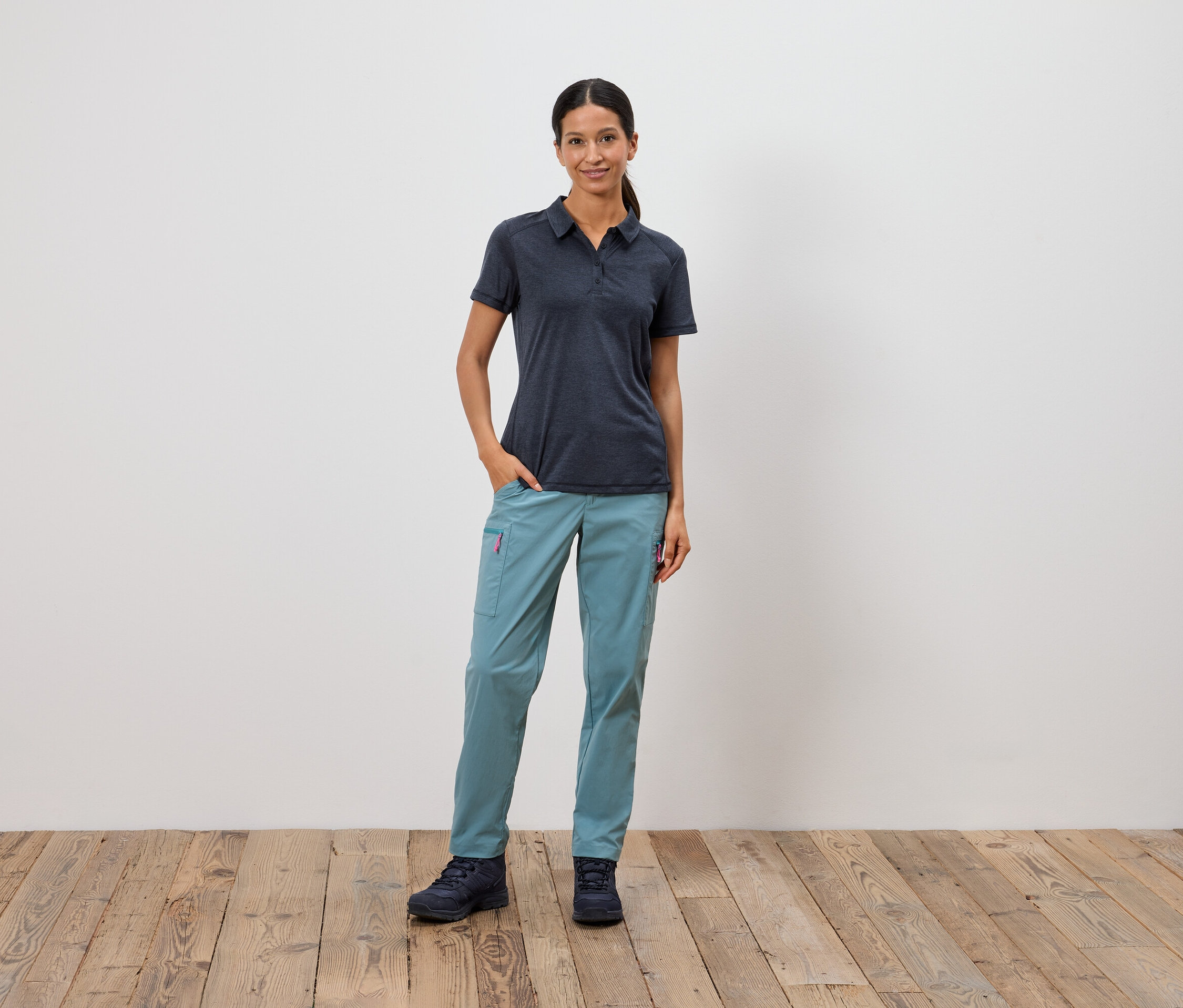 Žena stojí s rukou vo vrecku pred bielou stenou.