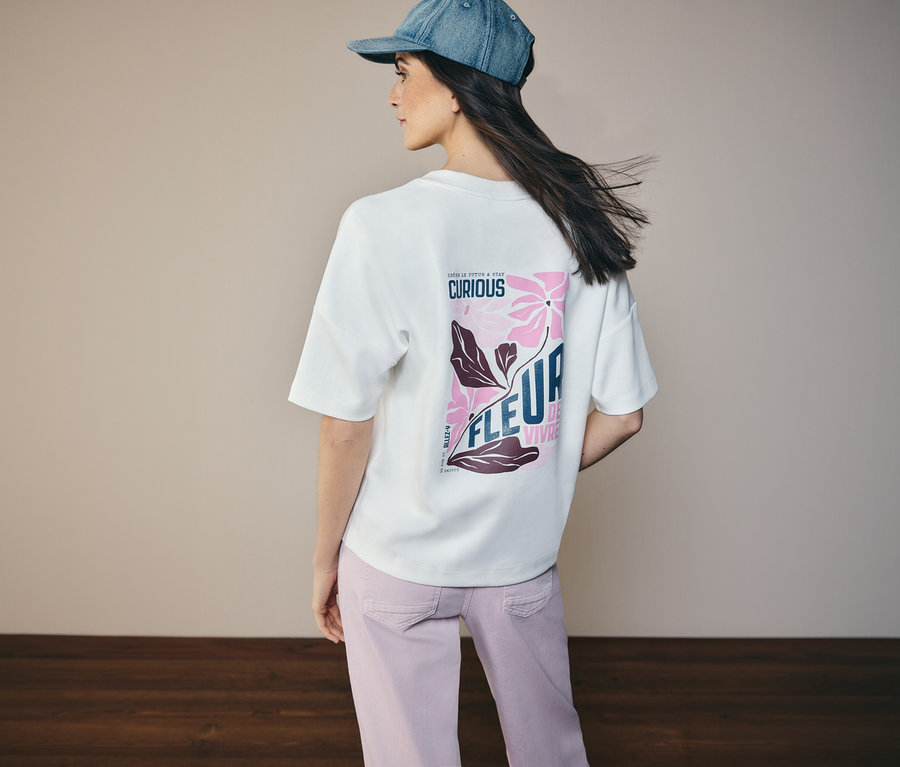 Žena zozadu v džínsovej bunde a tričku CECIL s kvetinovým vzorom na chrbte.