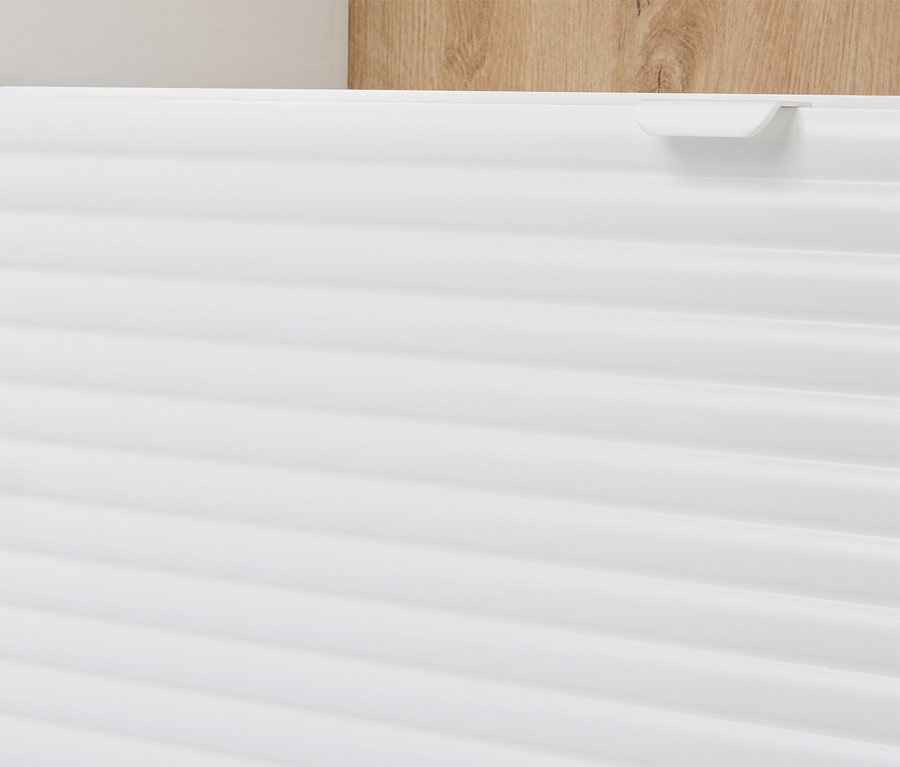 Detailný pohľad na bielu skrinku s horizontálnymi drážkami a svetlohnedým dreveným prvkom v pozadí.