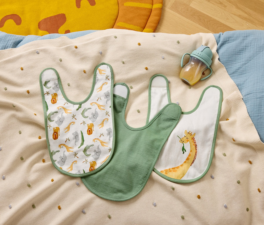 Tri podbradníky a fľaša na pitie ležia na béžovej deke s farebnými bodkami.