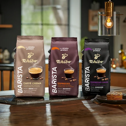 Tri balenia zrnkovej kávy Tchibo Barista stoja na stole, zľava doprava: Caffè Crema, Espresso a Espresso Dark.