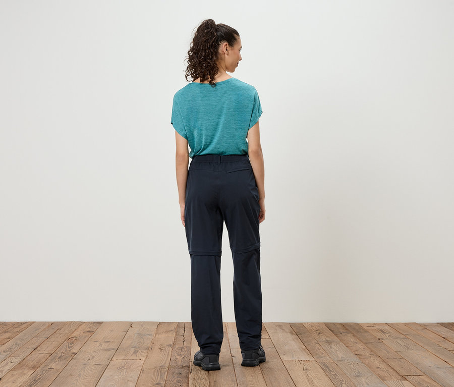 Žena stojí chrbtom k fotoaparátu, má na sebe modré tričko a tmavé nohavice so zipsom.