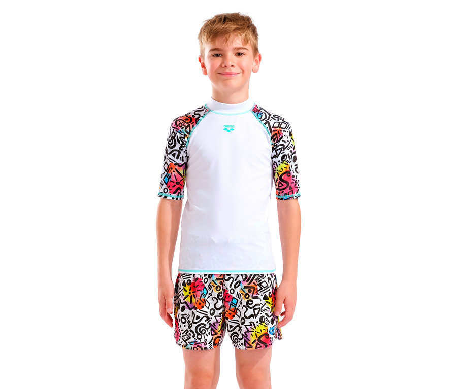 Chlapec s blond vlasmi má na sebe biely top Arena s farebnými rukávmi a zodpovedajúce šortky.