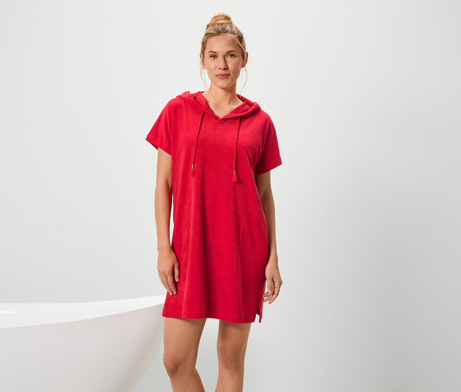 Žena stojí vedľa vane a má na sebe červené šaty s krátkym rukávom a kapucňou.