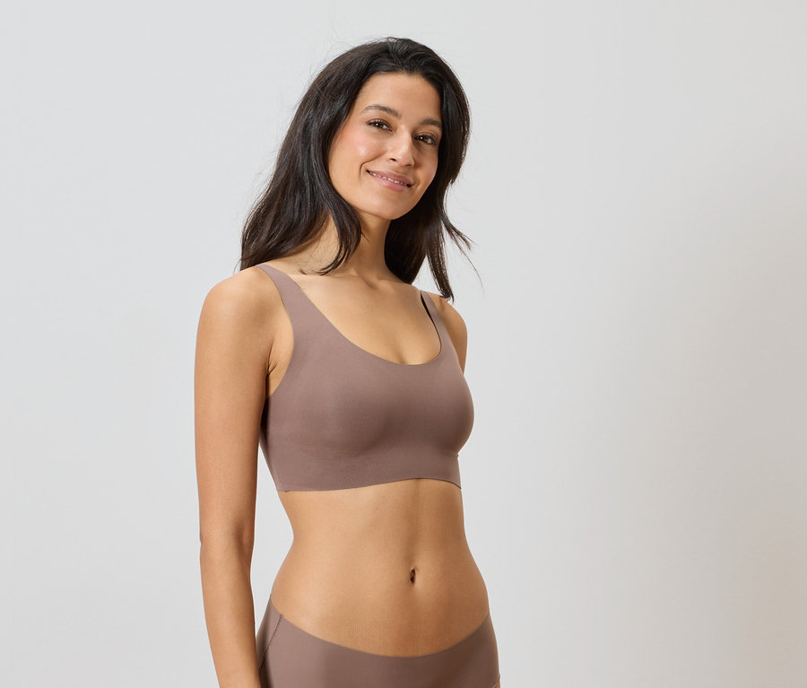 Žena má na sebe hnedú súpravu spodnej bielizne na neutrálnom pozadí.