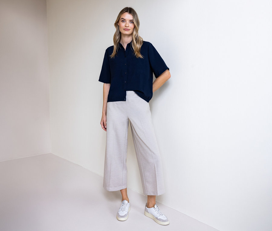 Žena v nohaviciach a košeľovej blúzke Street One. Stojí pred stenou.