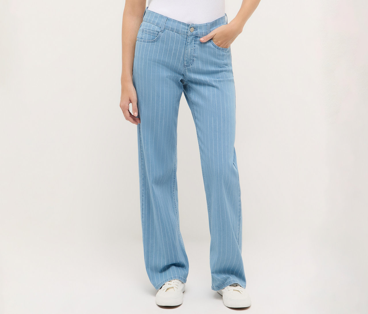 Žena má na sebe modré džínsy Angels Denim »Liz« Wide Leg s prúžkami a biele tenisky.