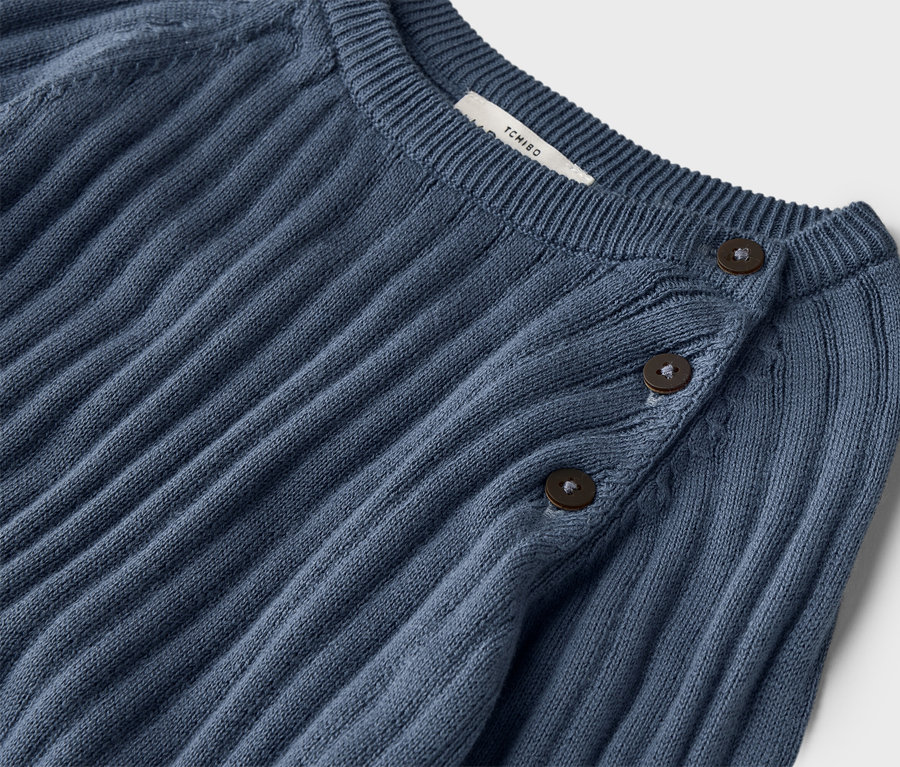 Detailný záber na rebrovaný, tmavomodrý pletený sveter s tromi gombíkmi pri krku.