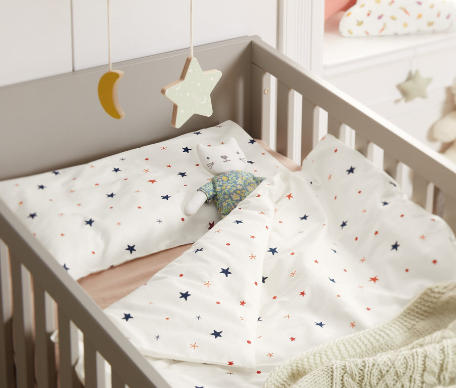 V postieľke je detská posteľná bielizeň s hviezdami a hračka mačky.