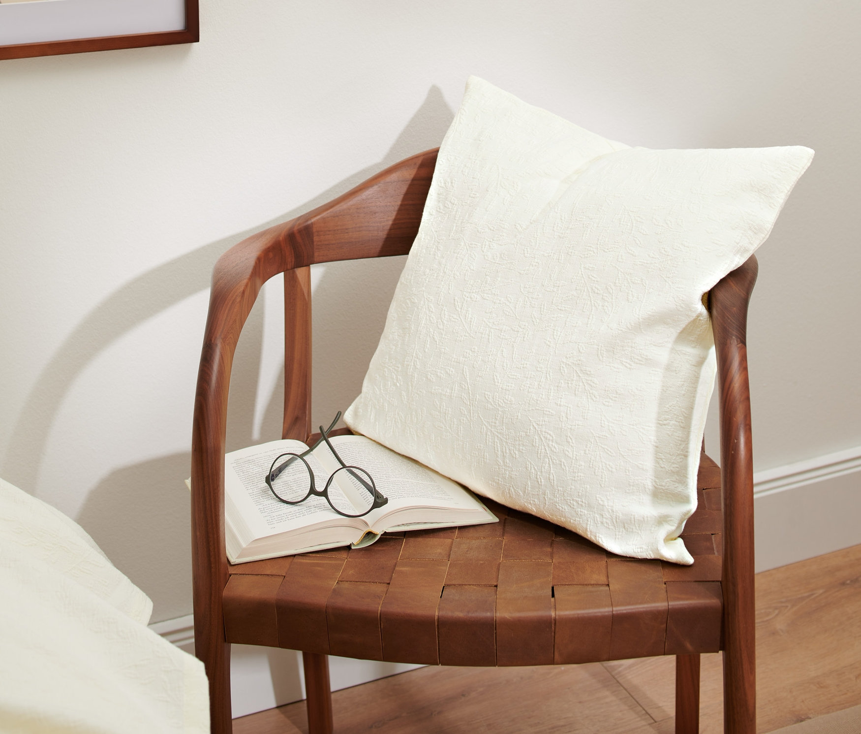 Na hnedej stoličke leží otvorená kniha, okuliare a krémová obliečka na dekoračný vankúš so žakárovou väzbou.