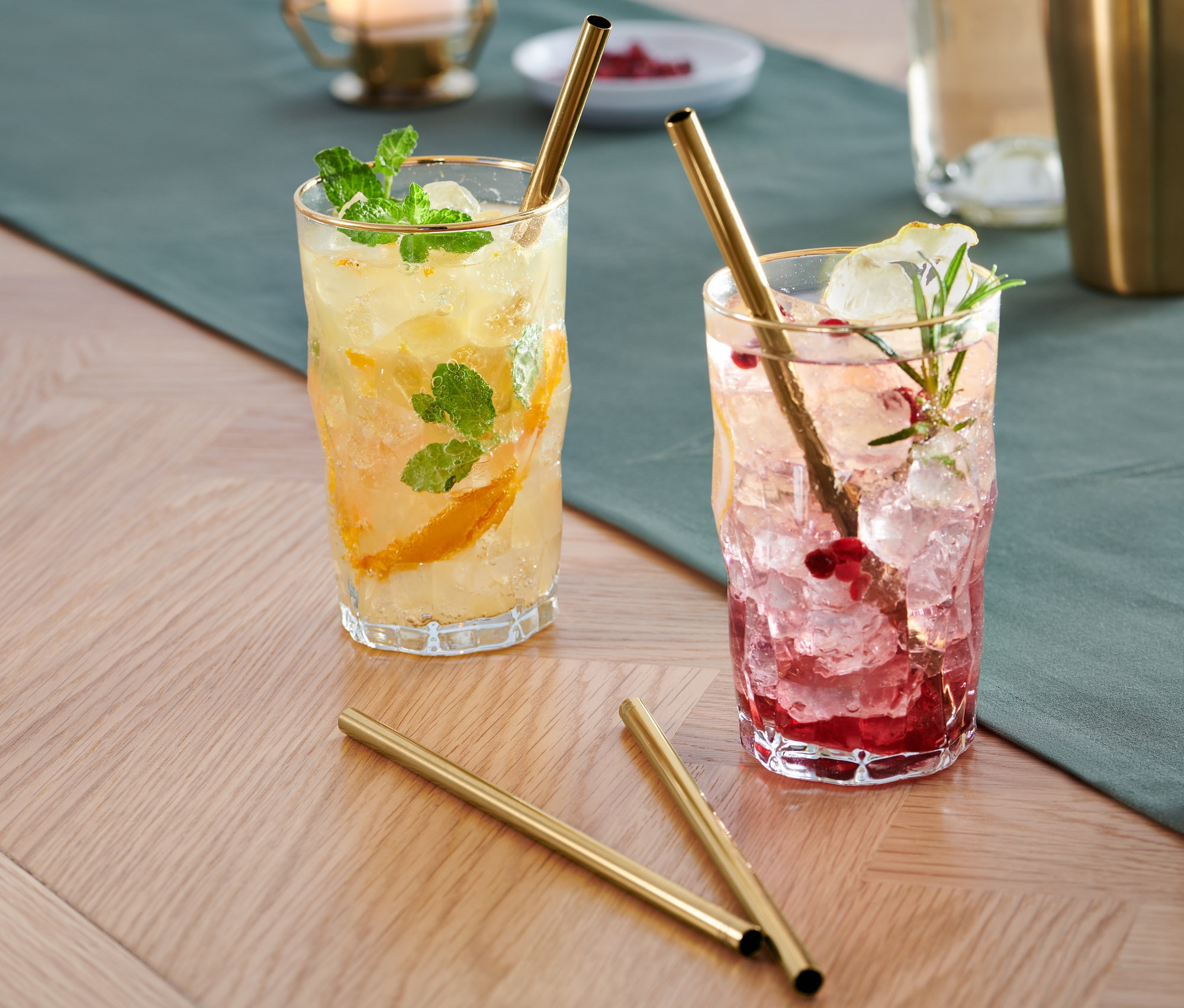 Dva nápoje s ľadom a ovocím v pohároch so zlatými Kovové slamky, 4 ks sú na stole.