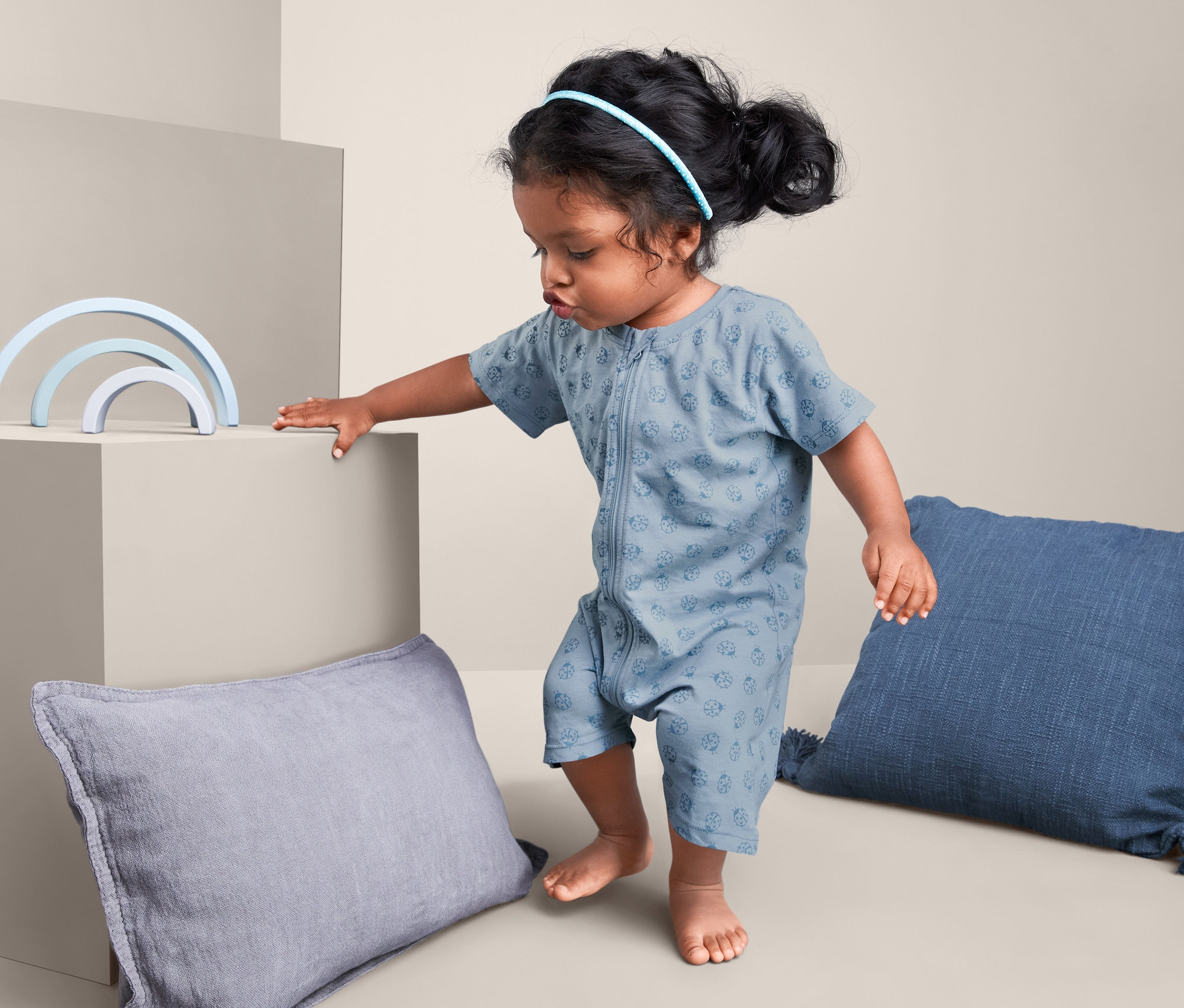 Dievčatko v krátkom pyžame, 2 ks, zeleno-modré, stojí vedľa modrej hračky a vankúšov.