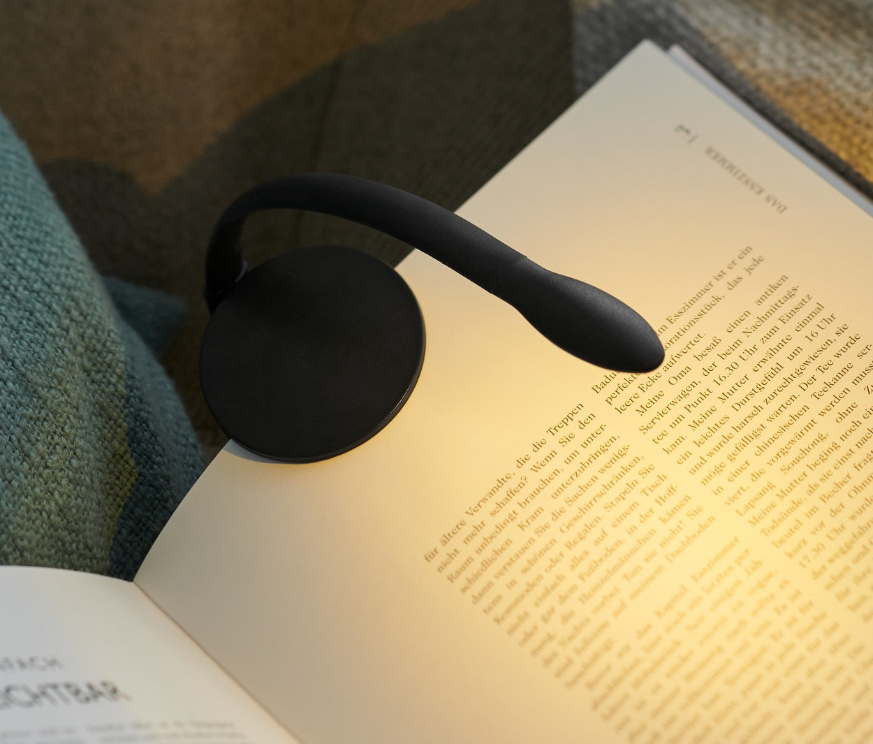 Čierna LED lampa na čítanie pripevnená na otvorenej knihe na kresle.