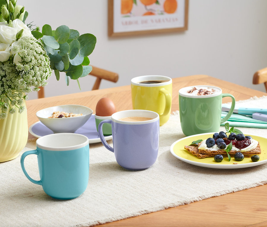 Štyri hrnčeky rôznych farieb stoja na stole s jedlom.