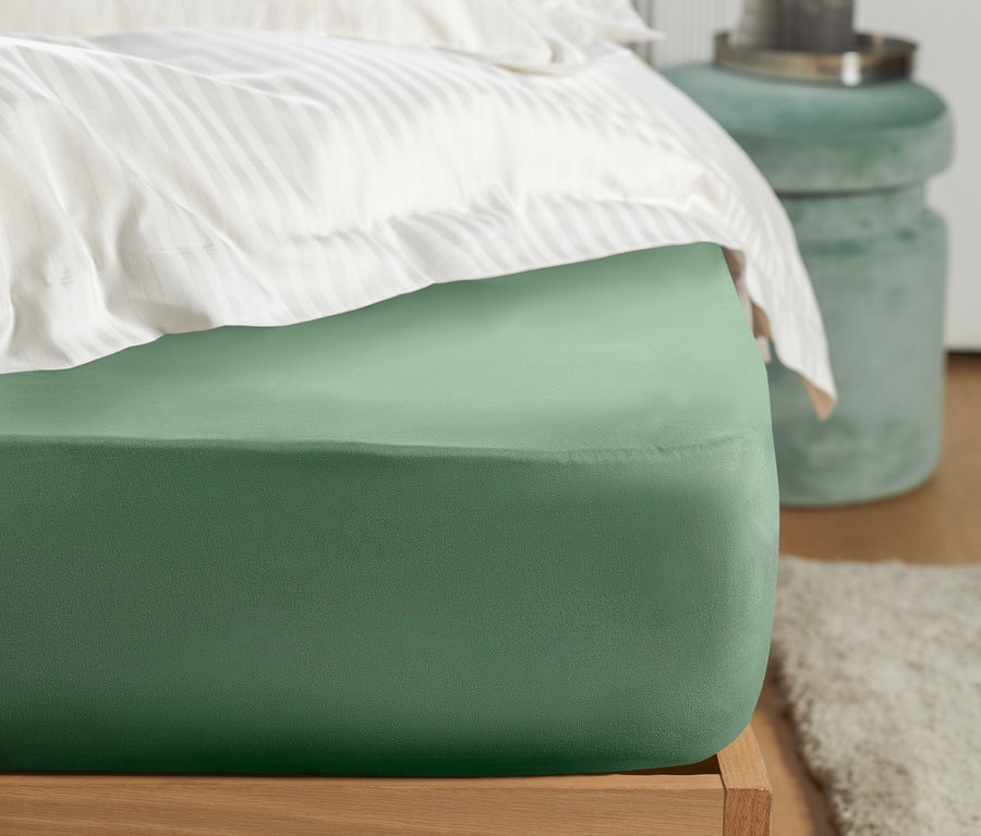 Detailný pohľad na zelené džersejové napínacie prestieradlo na posteli s bielymi pruhovanými vankúšmi.