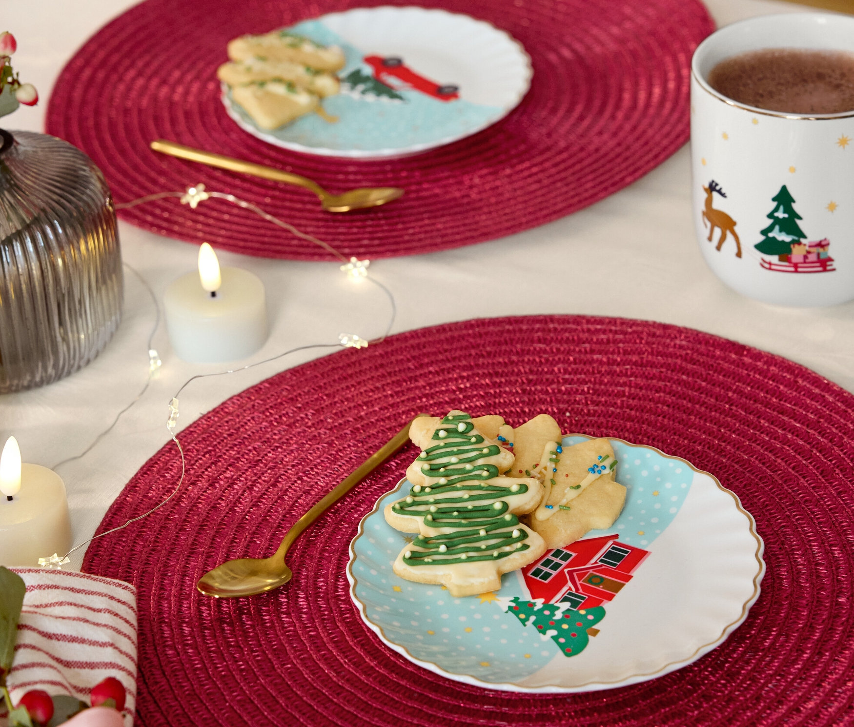 Dva stoly s červenými prestieraním, na nich dezertné taniere so zlatým dekorom, vykrajované sušienky a zlaté lyžičky.