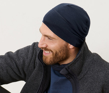 Muž sedí na drevenej podlahe a má na sebe čiapku s vlnou.