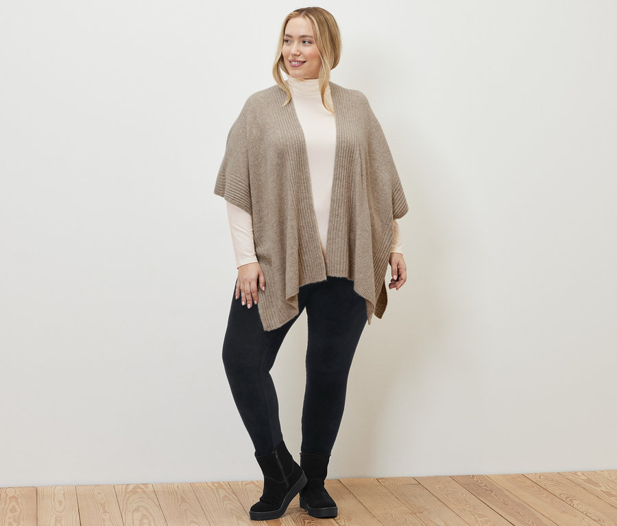 Žena má na sebe pletenú pelerínu, menčestrové legínsy a krémovobiele tričko s rolákovým golierom.