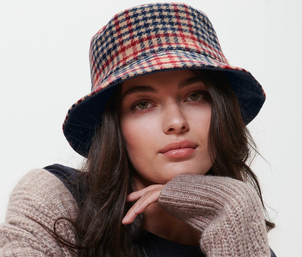 Žena sedí na stoličke a má na sebe obojstranný klobúk typu bucket hat.