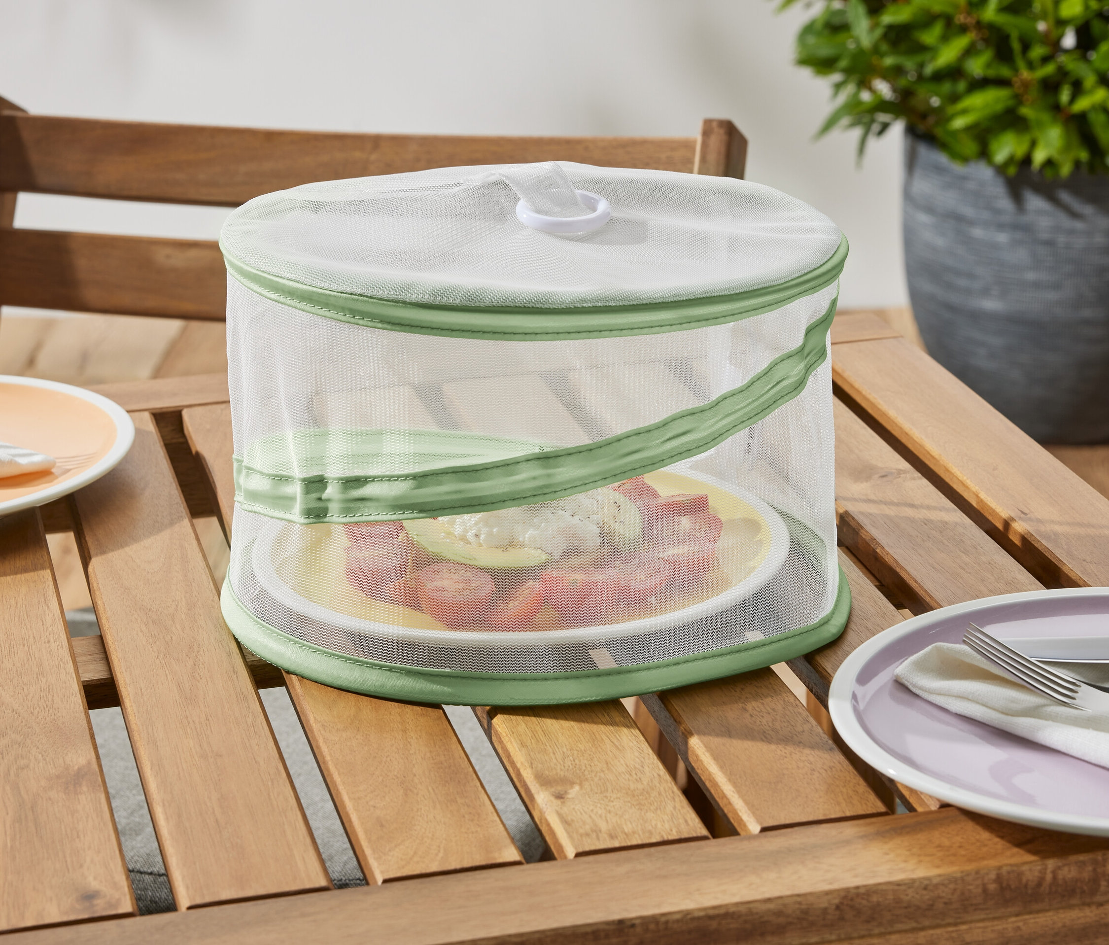 Skladací mini ochranný kryt stojí na drevenom stole a chráni tanier s jedlom.