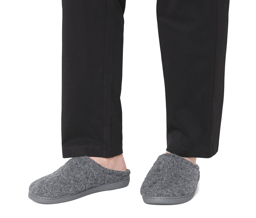 Nohy v čiernych nohaviciach a sivých papučiach.