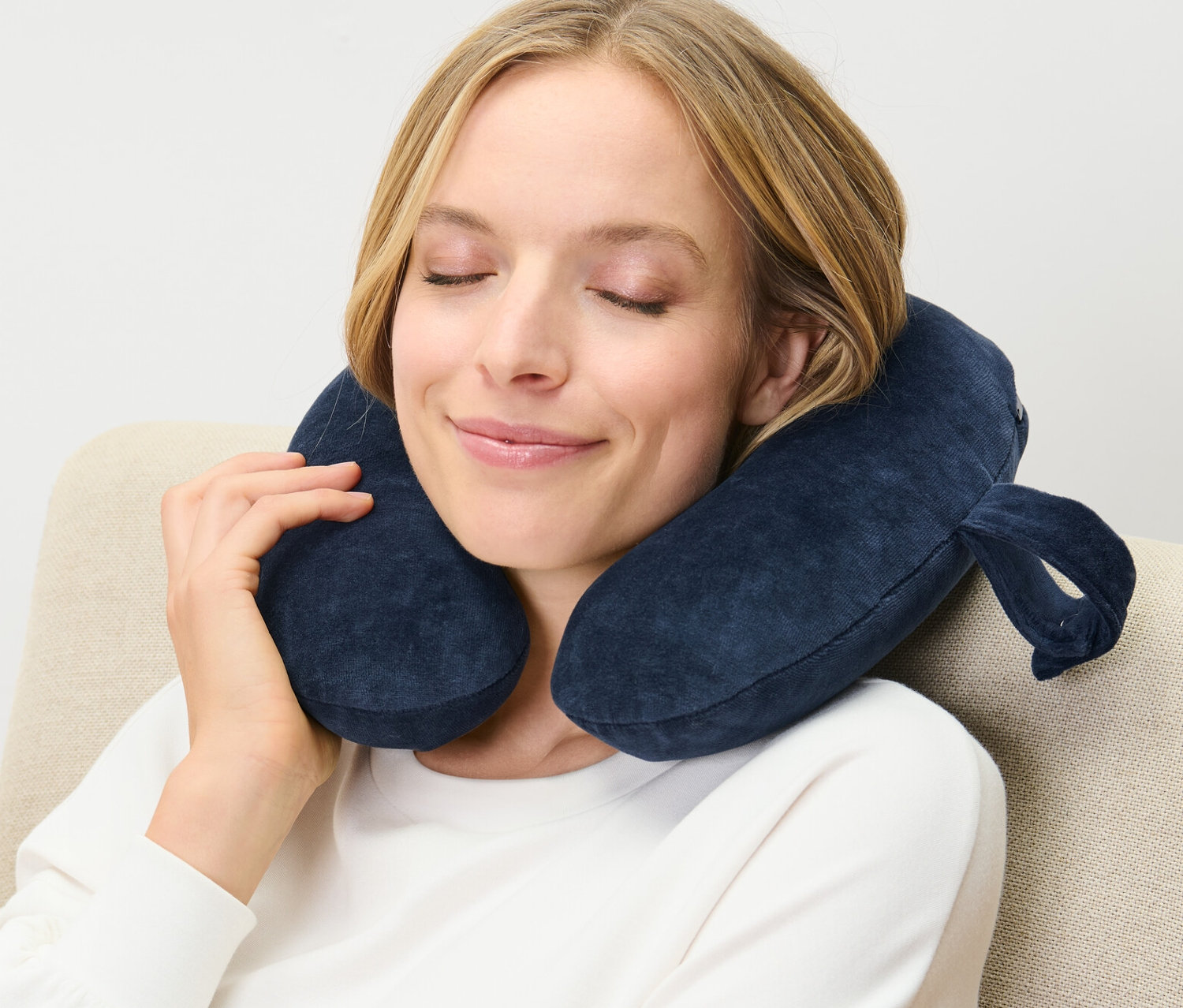 Žena sedí v kresle s tmavomodrým krčným vankúšom z pamäťovej peny okolo krku.