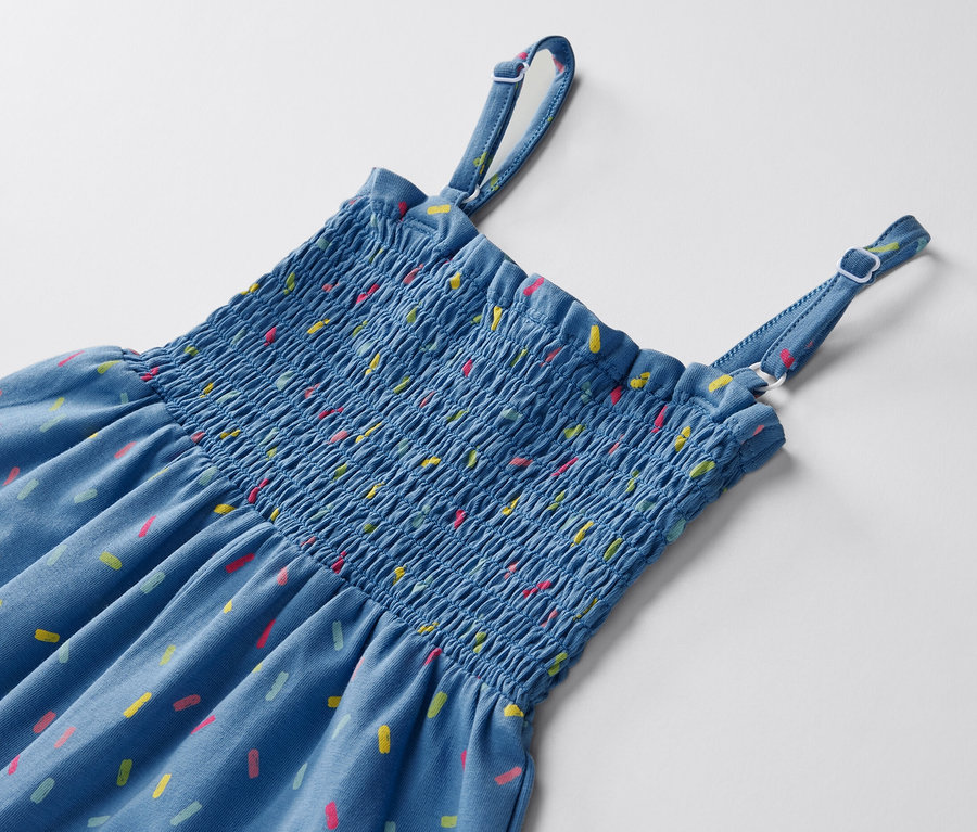 Detail modrého overalu v sedemosminovej dĺžke s farebnými vzormi na bielom pozadí.