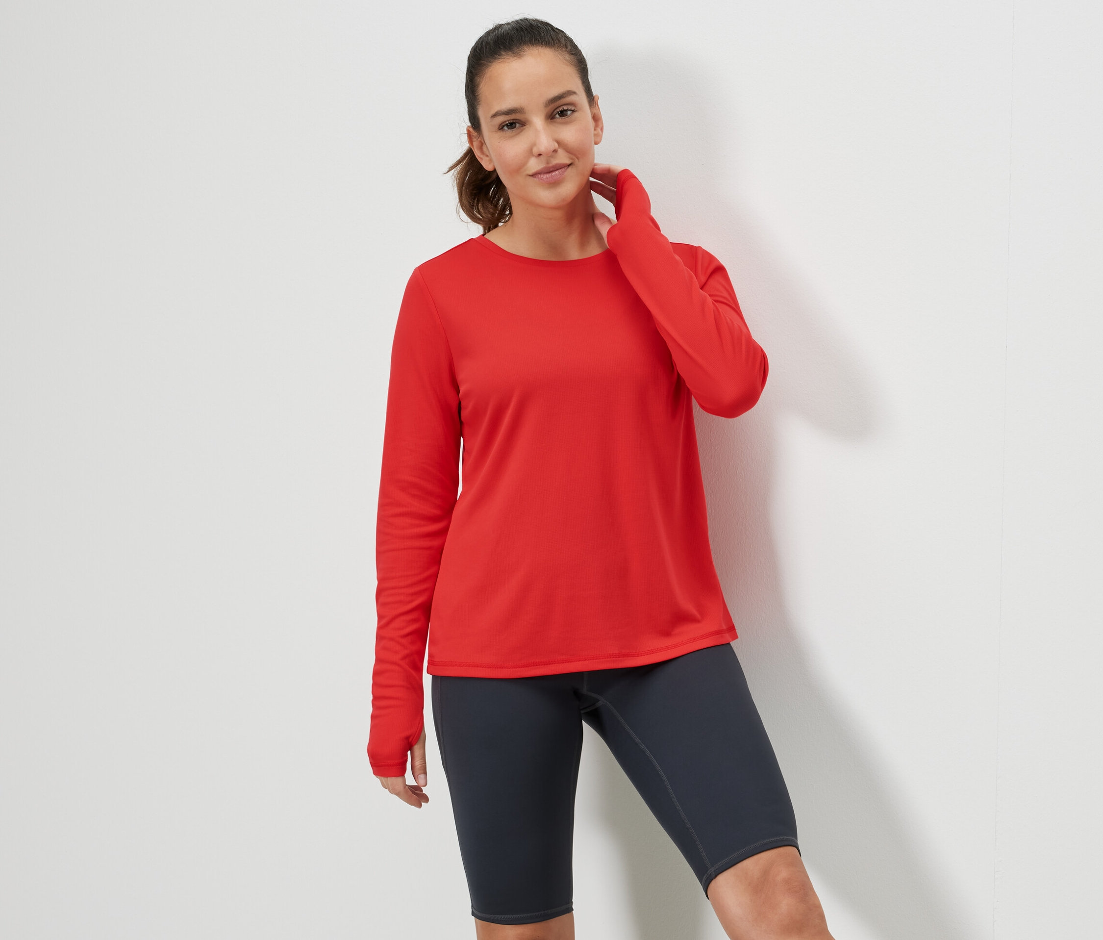 Žena pózuje v červenom športovom tričku s dlhým rukávom.