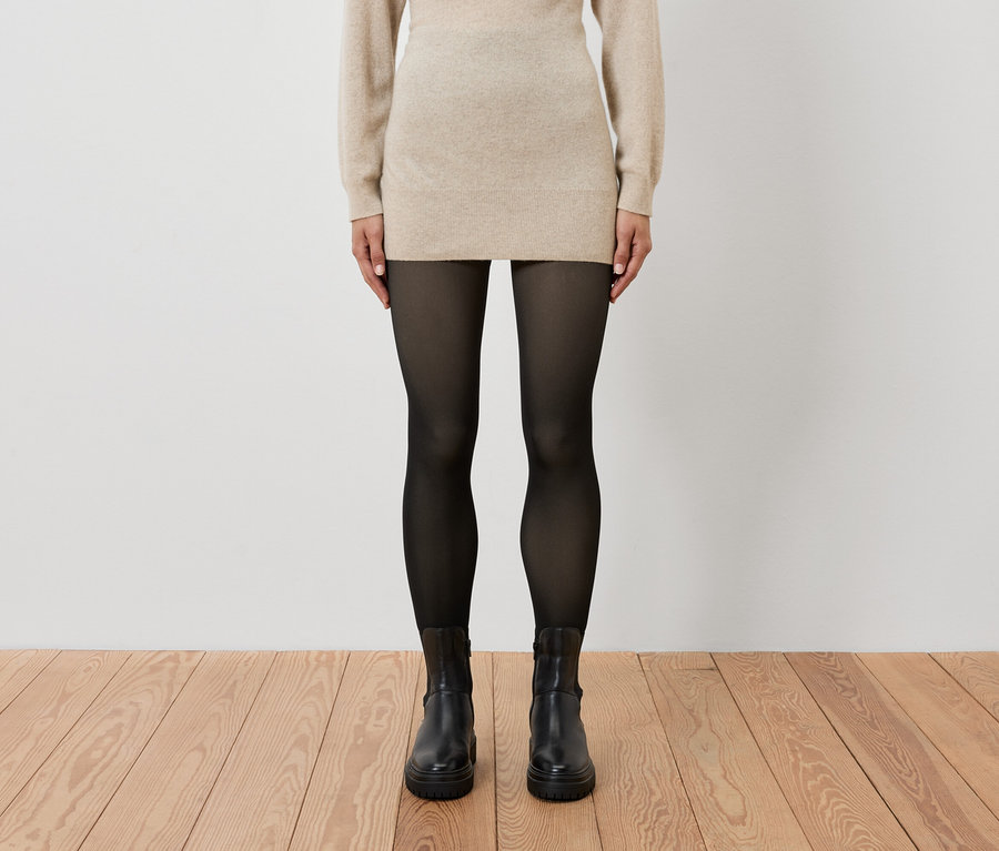 Žena má na sebe béžové šaty, čierne pančuchy a čierne topánky.