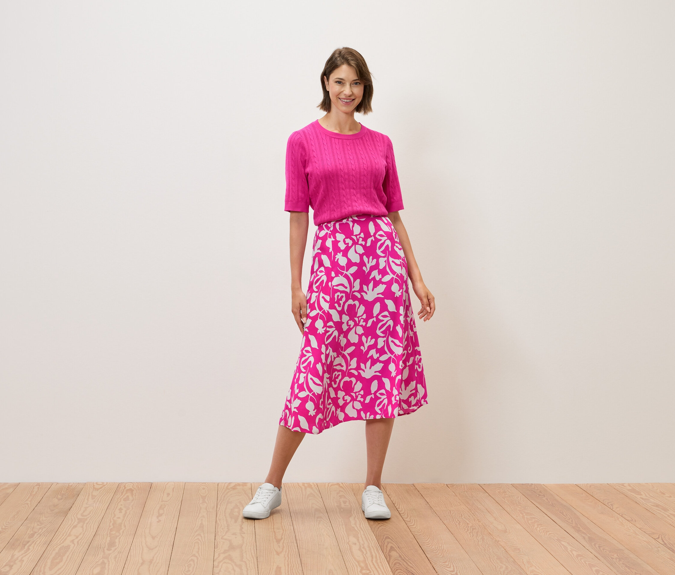 Žena stojí a má na sebe ružový top a sukňu s kvetinovým vzorom.