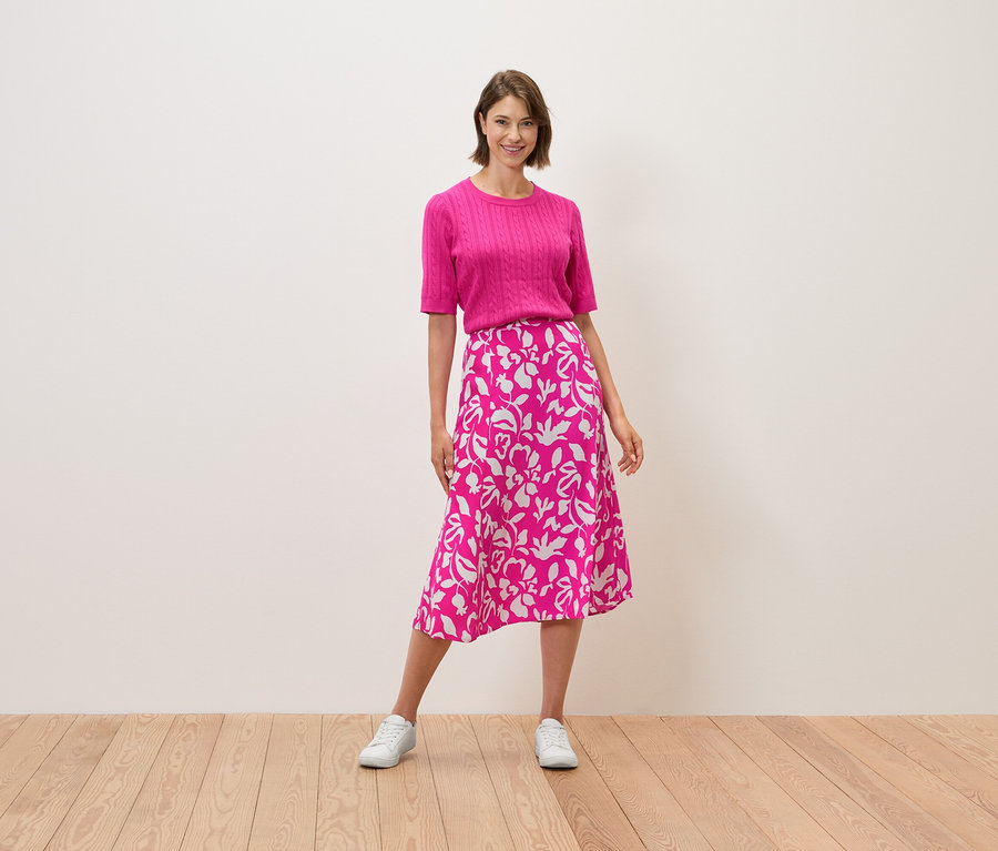 Žena stojí a má na sebe ružový top a sukňu s kvetinovým vzorom.