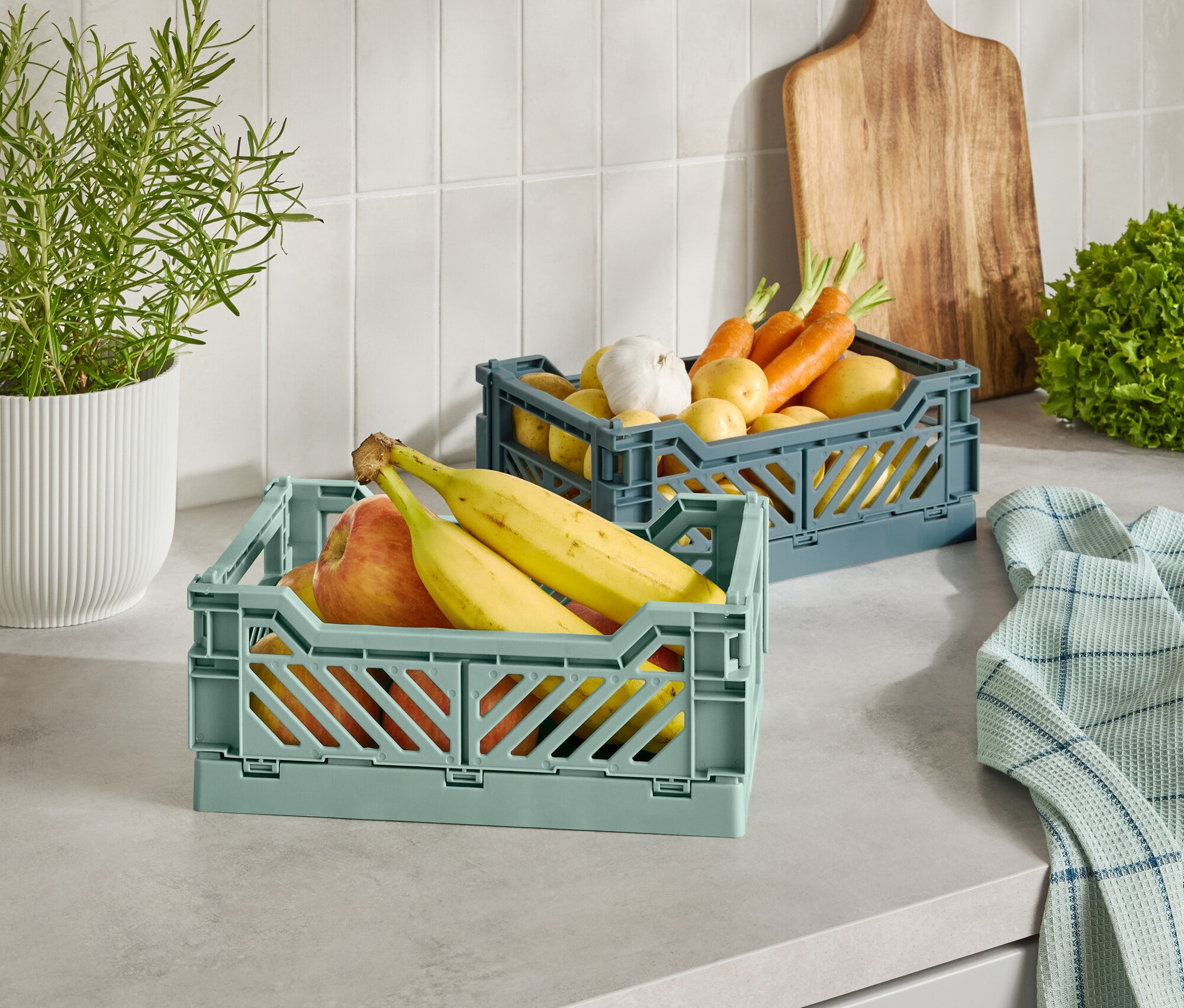 Dva plastové košíky s ovocím a zeleninou na kuchynskej linke.