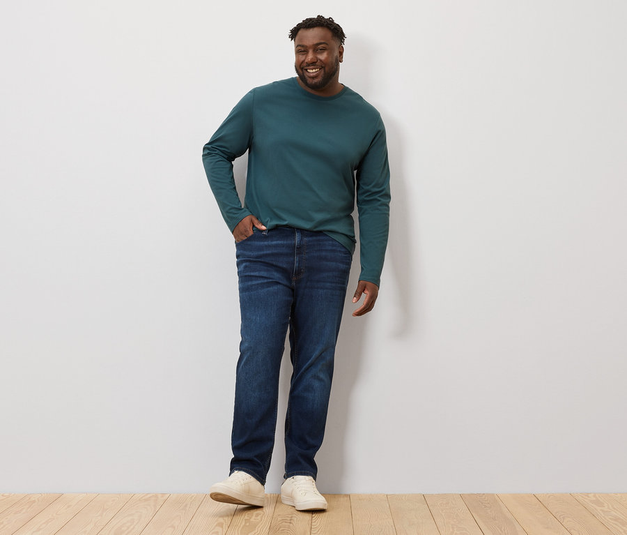 Muž pózuje v zelenom tričku s dlhým rukávom a džínsoch. Má na sebe 2 ks tričiek s dlhými rukávmi.