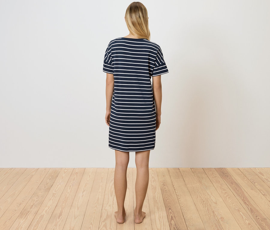 Žena stojí chrbtom k fotoaparátu a má na sebe modro-biele pruhované tričkové šaty.