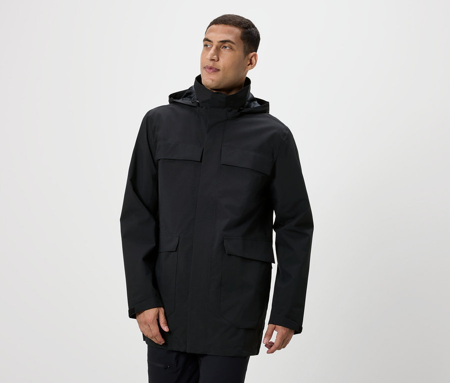 Muž pózuje v čiernej bunde s kapucňou a vreckami.