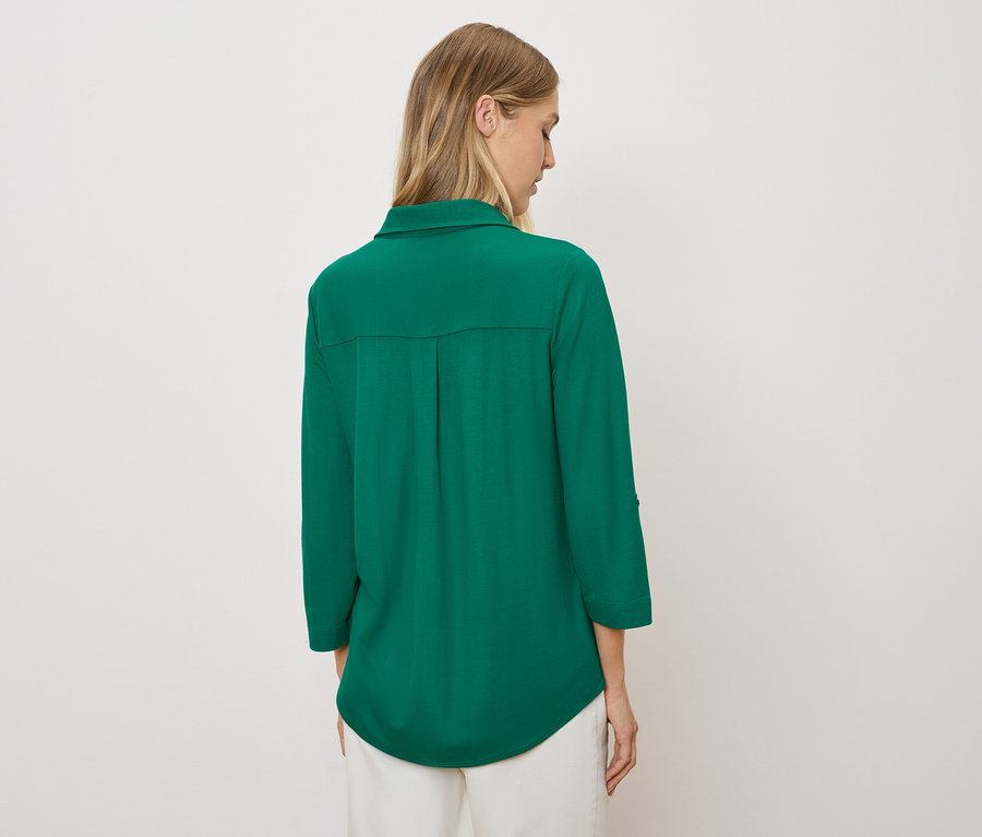 Žena chrbtom k fotoaparátu má na sebe zelenú košeľu a biele nohavice.