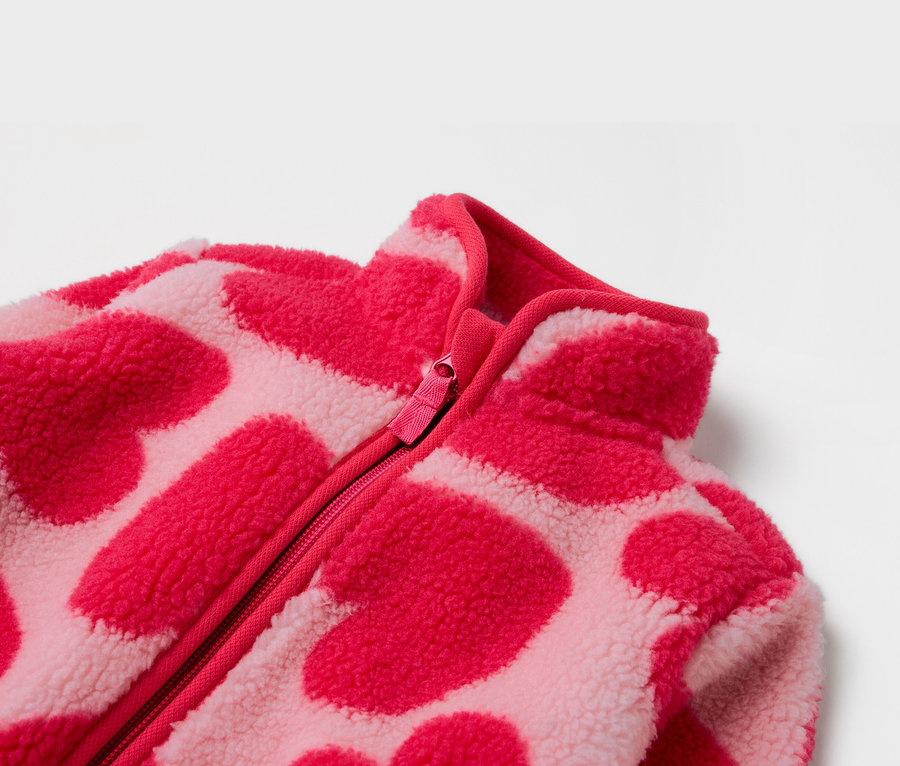 Detail ružovej fleecovej bundy so zipsom a vzorom sŕdc.