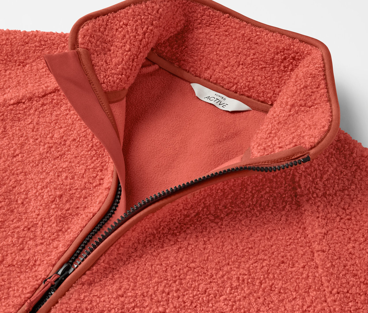 Detailný pohľad na koralovú fleecovú mikinu so zipsom.