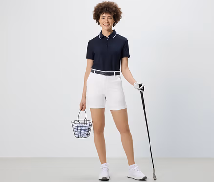 Žena drží košík s golfovými loptičkami a golfovou palicou. Má na sebe biele softshellové funkčné šortky.
