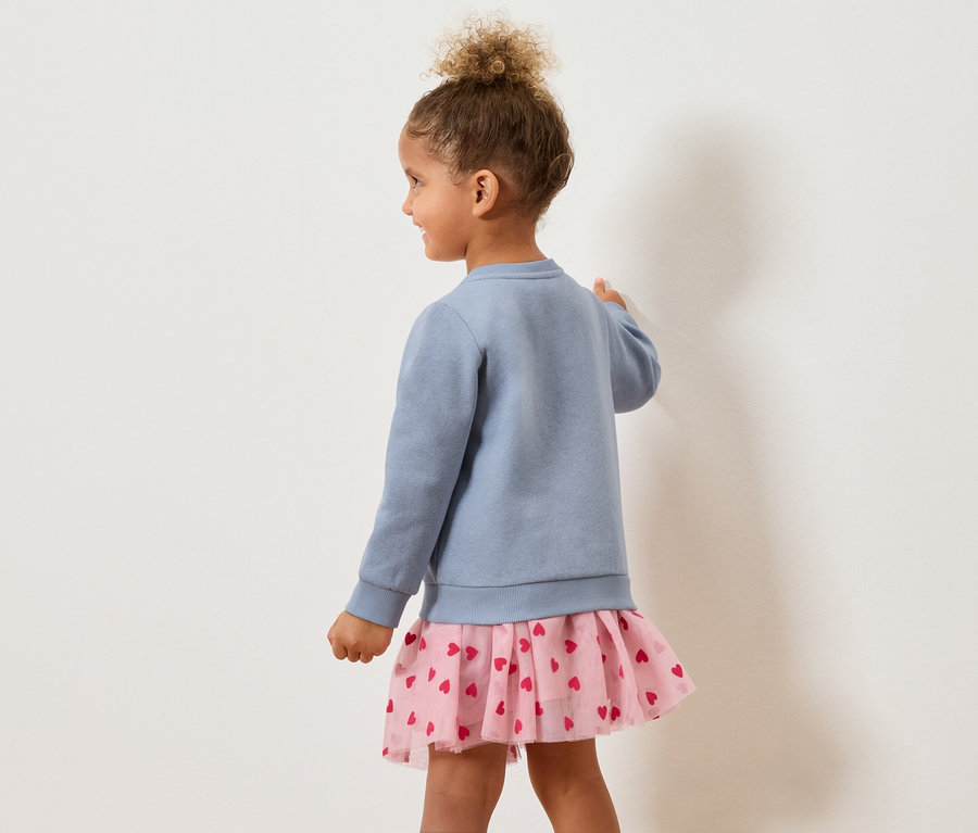 Dievča zozadu v modrom svetri a ružovej sukni so srdiečkami.