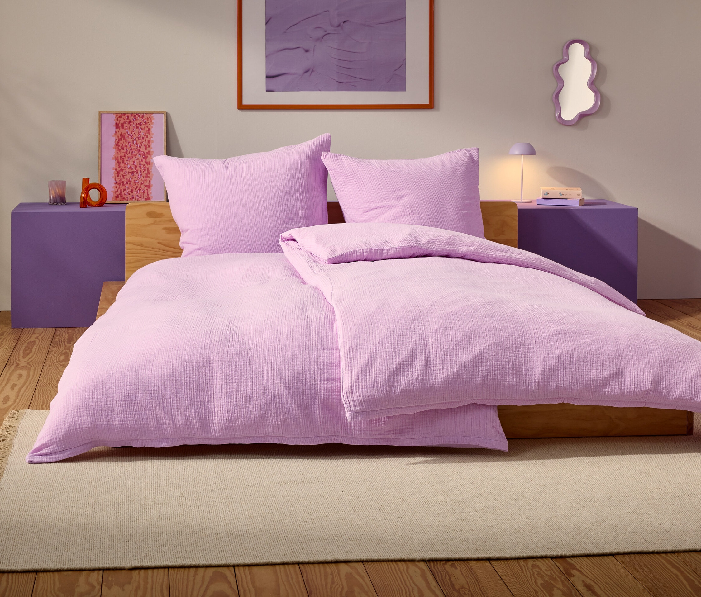 Fialová posteľ s dvoma vankúšmi a prikrývkou stojí na béžovom koberci v spálni.