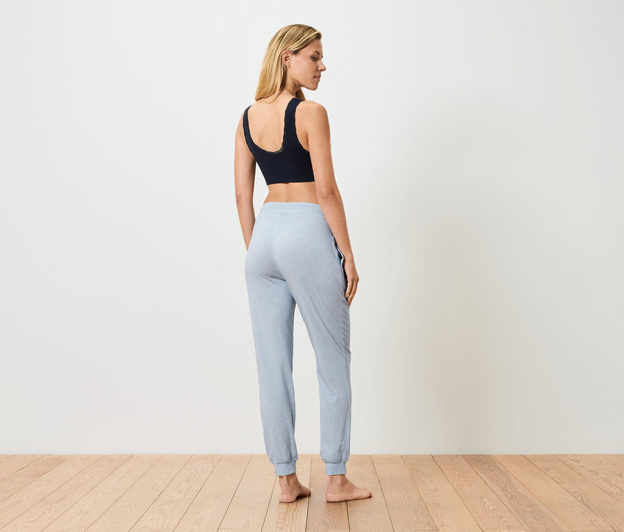 Žena stojí chrbtom, má na sebe čiernu športovú podprsenku a svetlomodré tepláky.