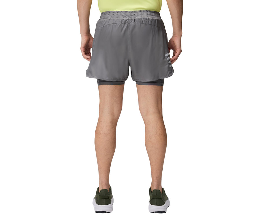 Muž zozadu v sivých šortkách a zelených topánkach.