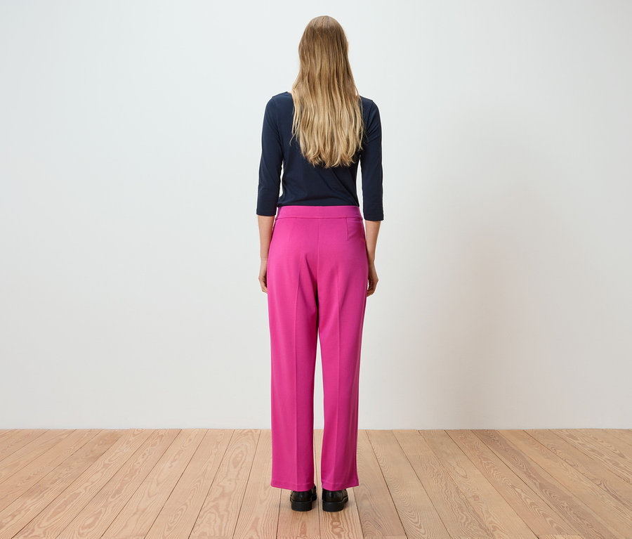 Pohľad zozadu na ženu s dlhými blond vlasmi, ktorá má na sebe tmavomodré tričko s dlhým rukávom a ružové nohavice.