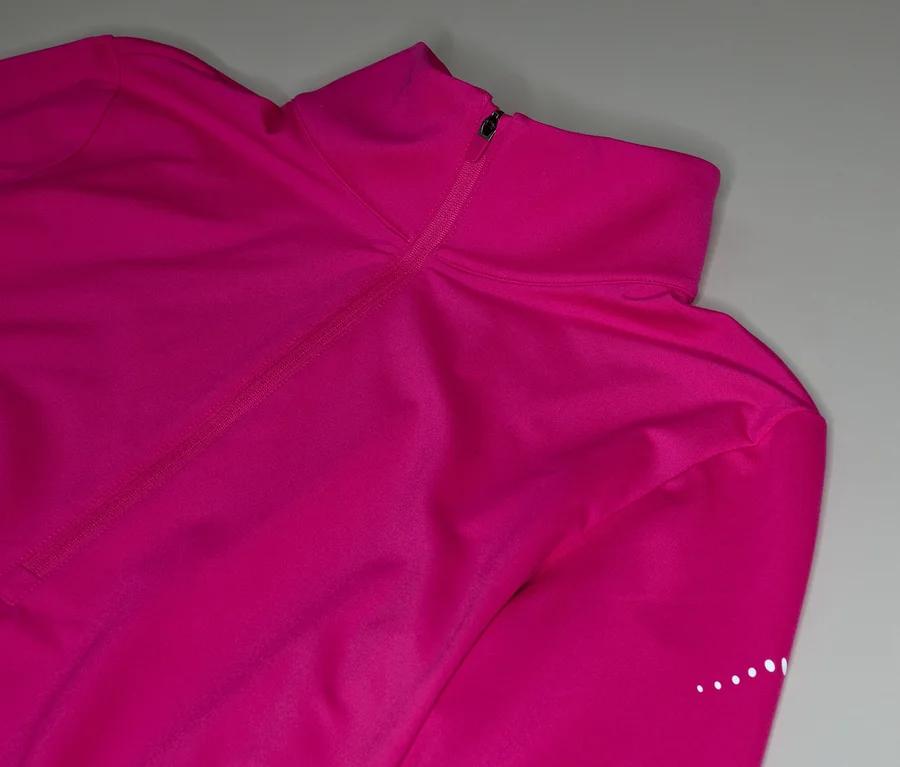 Detail ružového trička s dlhým rukávom, golierom na zips a reflexnými bodkami na rukáve.