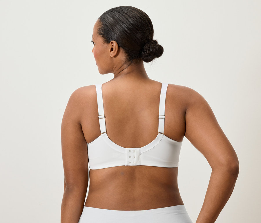 Pohľad zozadu na ženu s drdolom vo vlasoch, ktorá má na sebe bielu podprsenku a spodnú bielizeň.