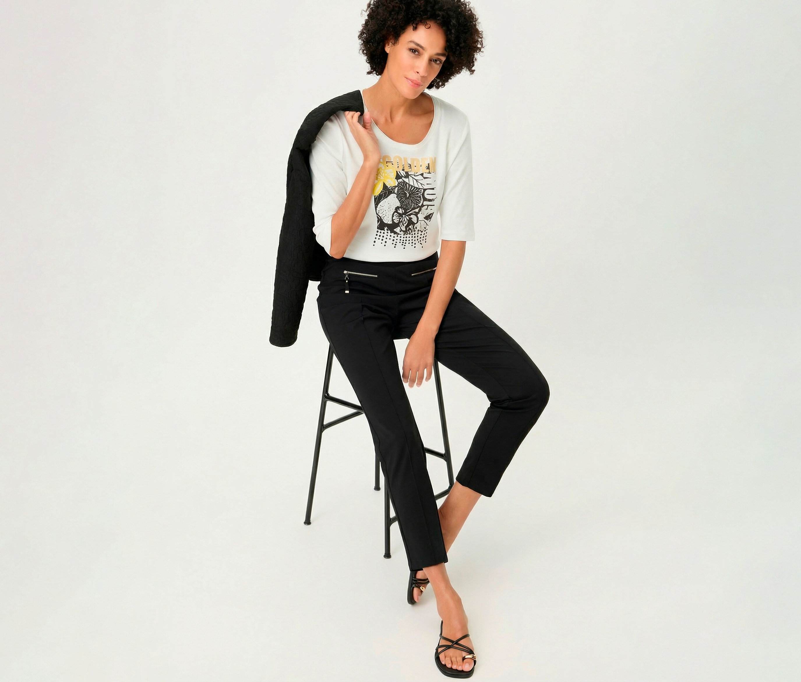 Žena sedí na stoličke v 3/4 tričku Olsen a má sako prehodené cez rameno.